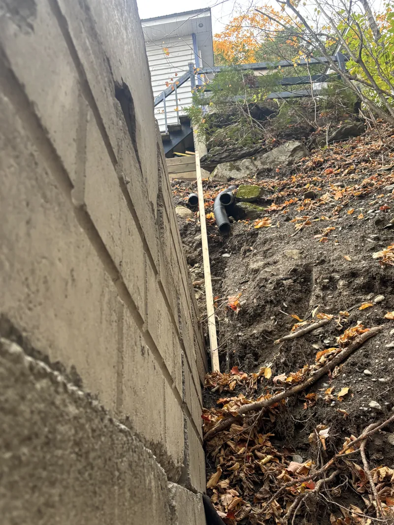 Arrière d'un mur de soutènement en blocs de béton, avec tuyaux de drainage annelés noirs sortant de la pente Arrière d'un mur de soutènement en blocs de béton, avec tuyaux de drainage annelés noirs sortant de la pente