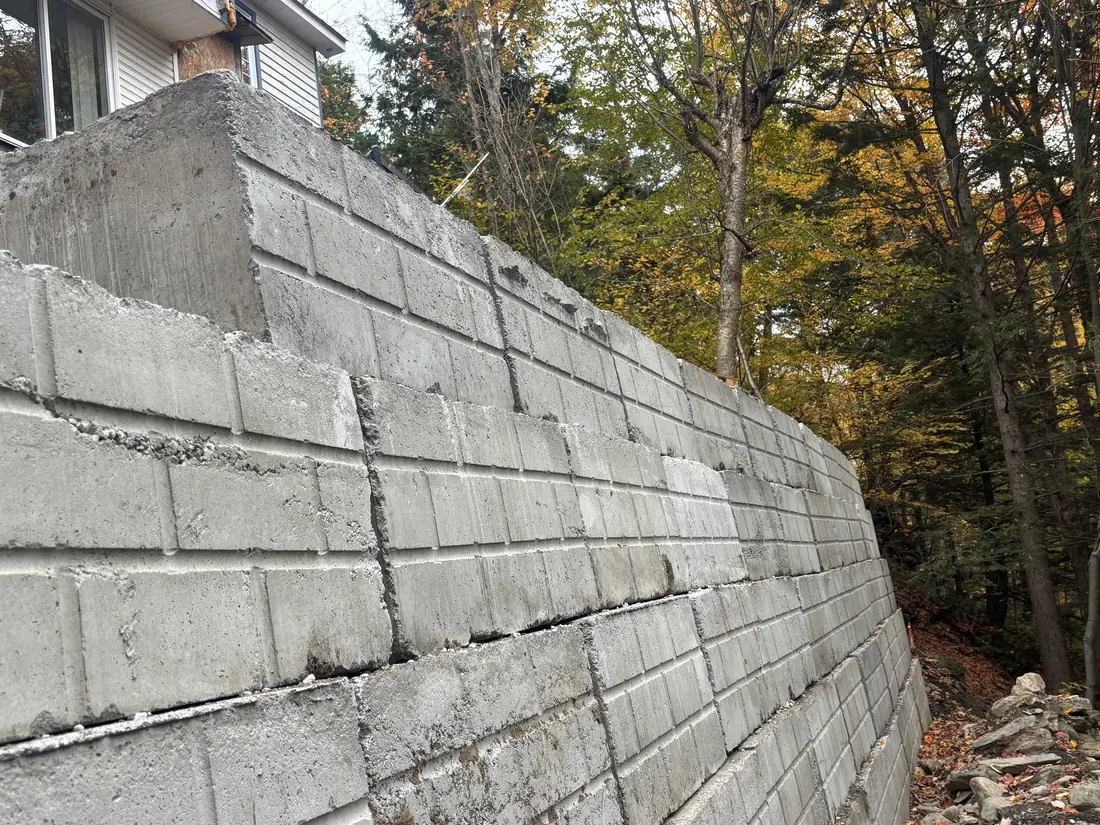 Long mur de soutènement en gros blocs de béton à face rainurée, posés en rangs superposés le long d'un terrain boisé Long mur de soutènement en gros blocs de béton à face rainurée, posés en rangs superposés le long d'un terrain boisé