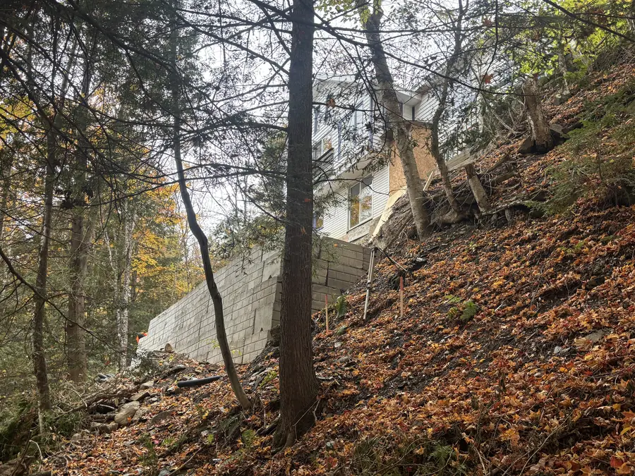 Mur de soutènement en blocs de béton vu du bas d'un terrain boisé à forte pente, sous une maison Mur de soutènement en blocs de béton vu du bas d'un terrain boisé à forte pente, sous une maison