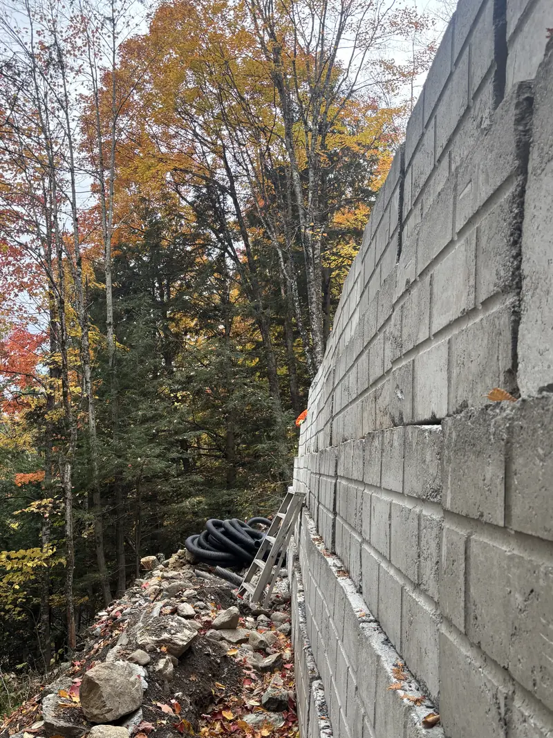 Vue en longueur d'un mur de soutènement en blocs de béton, avec rouleau de tuyau de drainage et pierres au pied du mur, en forêt Vue en longueur d'un mur de soutènement en blocs de béton, avec rouleau de tuyau de drainage et pierres au pied du mur, en forêt